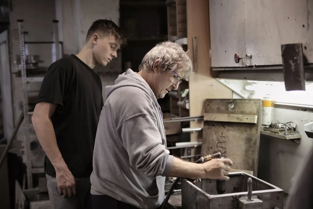 Professionnel expérimenté et apprenti manipulant une pièce sur un établi