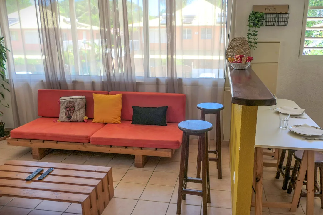Sala de apartamento em Caiena com sofá vermelho, banquetas e balcão