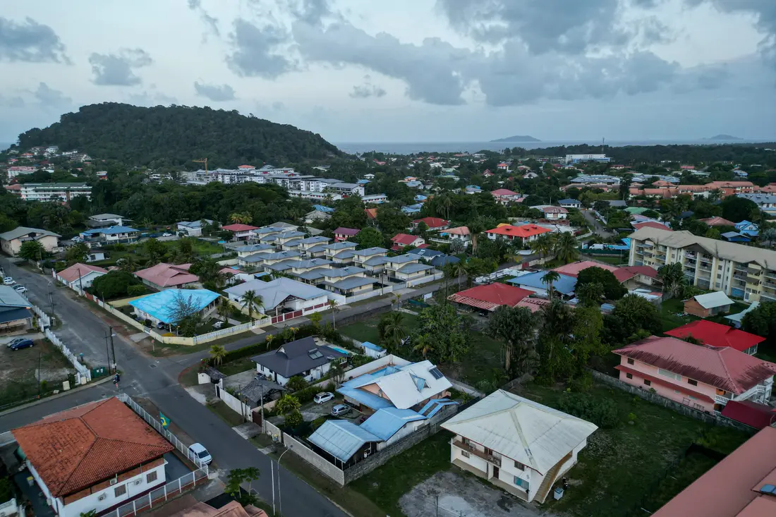 Vue aérienne de Cayenne au crépuscule : toits, végétation et colline de Montabo avec l’océan en toile de fond