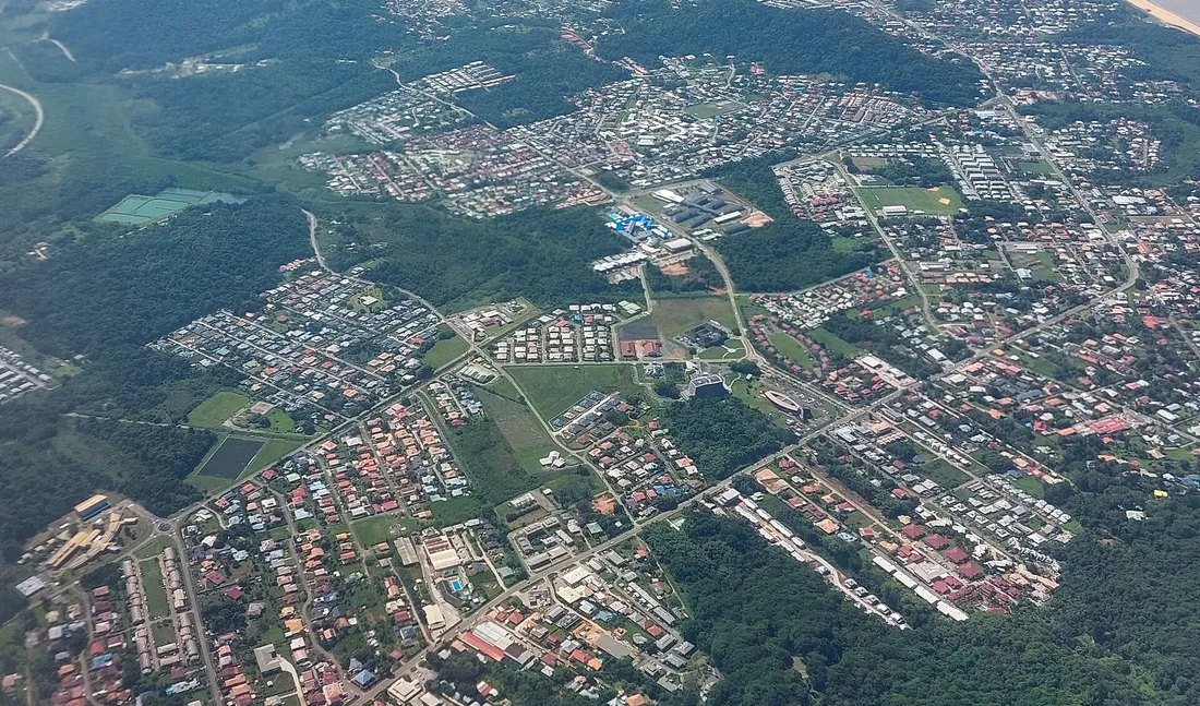 Vue aérienne oblique de Rémire-Montjoly et de la périphérie de Cayenne, en Guyane : lotissements pavillonnaires, rangées de petits immeubles récents, zones d'activité et parcelles boisées