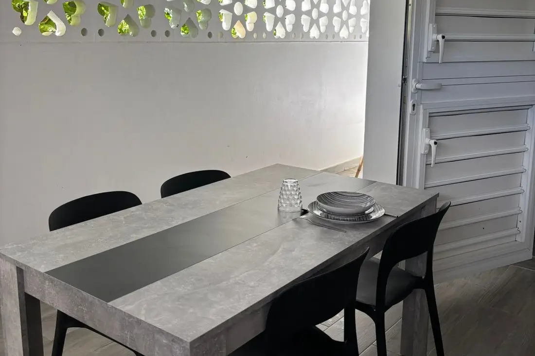 Salle à manger de la maison Tropikana : table grise dressée, chaises noires et claustra blanc ajouré