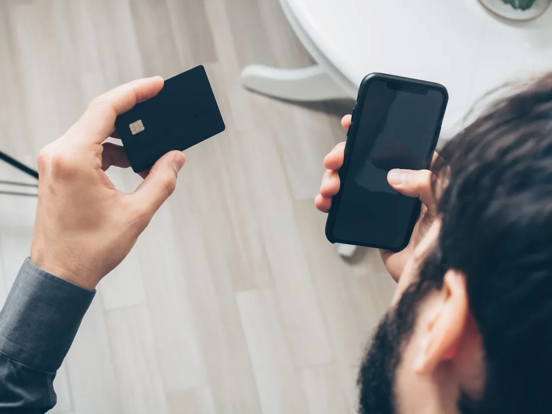 Nouvel arrivant tenant une carte bancaire dans une main et un smartphone dans l'autre, symbolisant l'ouverture d'un compte et d'une ligne mobile