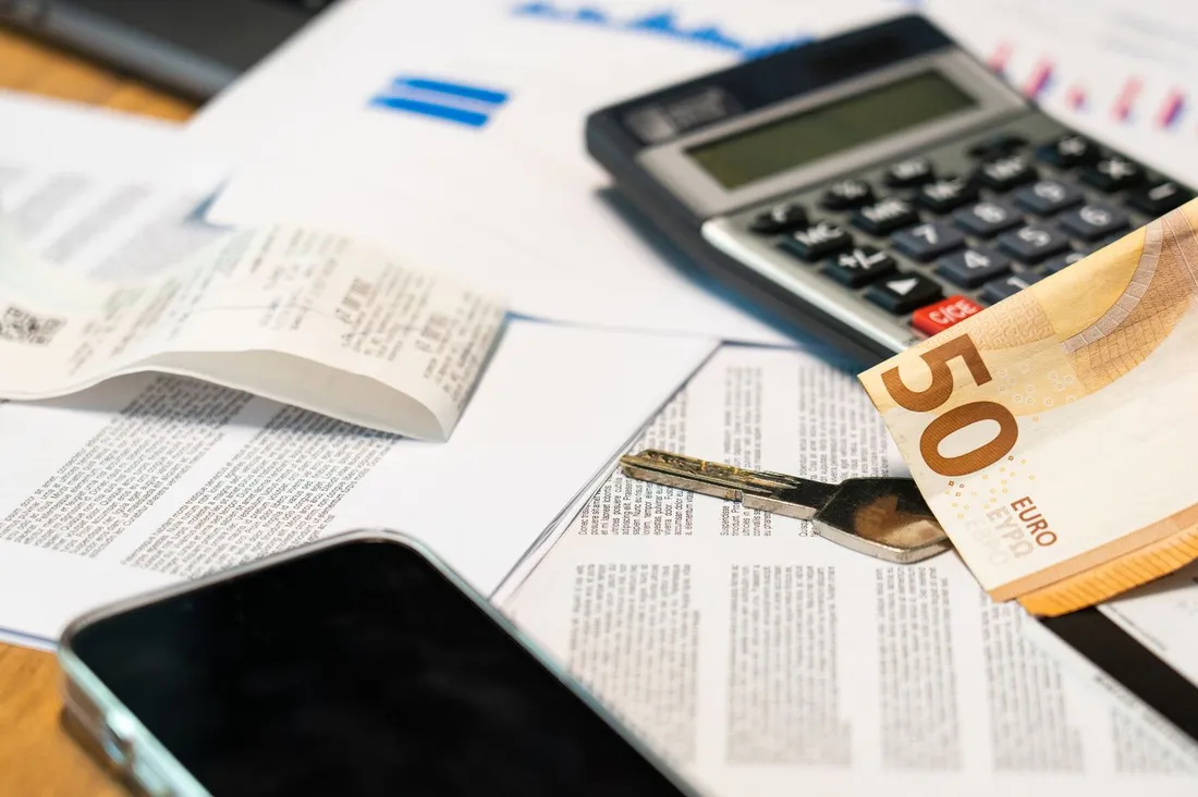 Calculatrice, billet de 50 euros, clé et documents financiers posés sur un bureau