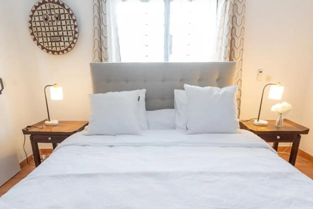 Chambre de la Casa Belas Artes : grand lit blanc à tête capitonnée grise, chevets en bois et lampes allumées