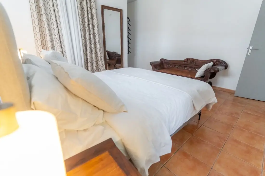 Autre chambre de la Casa Belas Artes : lit blanc, grand miroir sur pied et banc en bois sculpté