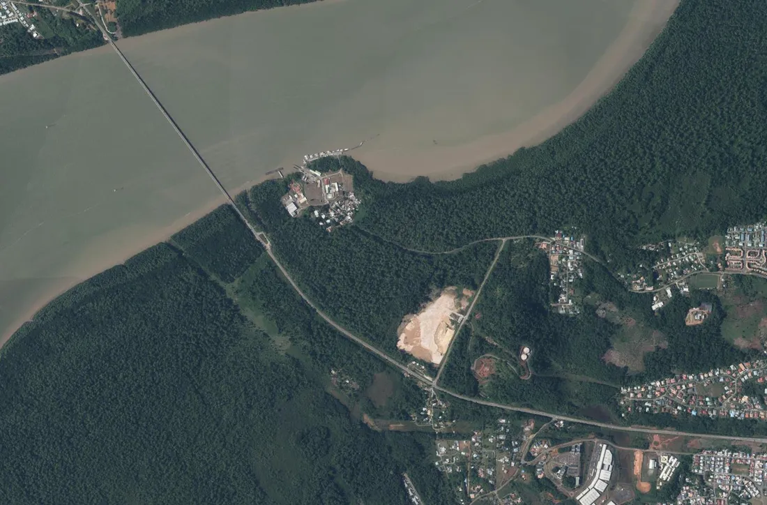 Vue aérienne du Larivot, à Matoury : le pont de la RN1 franchissant la rivière de Cayenne en haut à gauche, le port du Larivot et ses appontements sur la presqu'île, la plateforme claire de la future centrale ouverte dans la forêt au centre à droite