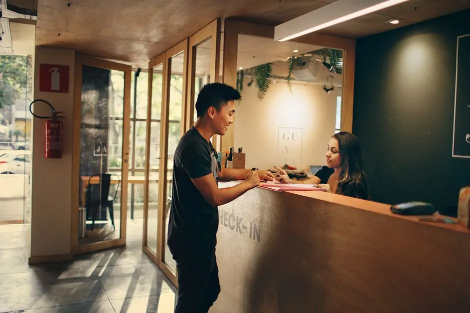 Voyageur accueilli au comptoir d'un hébergement portant la mention CHECK-IN, remise des clés à son arrivée