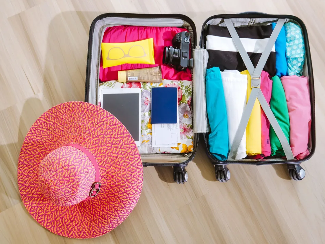Valise ouverte preparee avant le depart avec passeport, chapeau de soleil, creme solaire, appareil photo et vetements legers