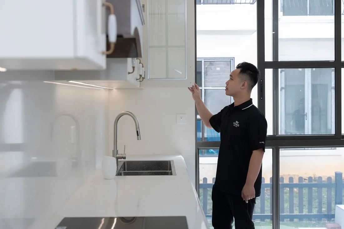 Visiteur inspectant un meuble de cuisine et l'évier dans un appartement lumineux avant la signature du bail
