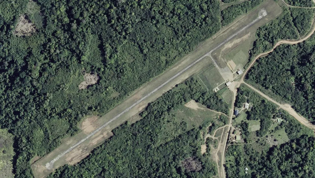 Vue aérienne verticale de la piste d'aviation de Maripasoula, en Guyane : bande revêtue rectiligne tracée en diagonale au milieu de la forêt, petite aérogare et aire de stationnement sur le côté, chemins de latérite ocre, aucune route goudronnée aux alentours