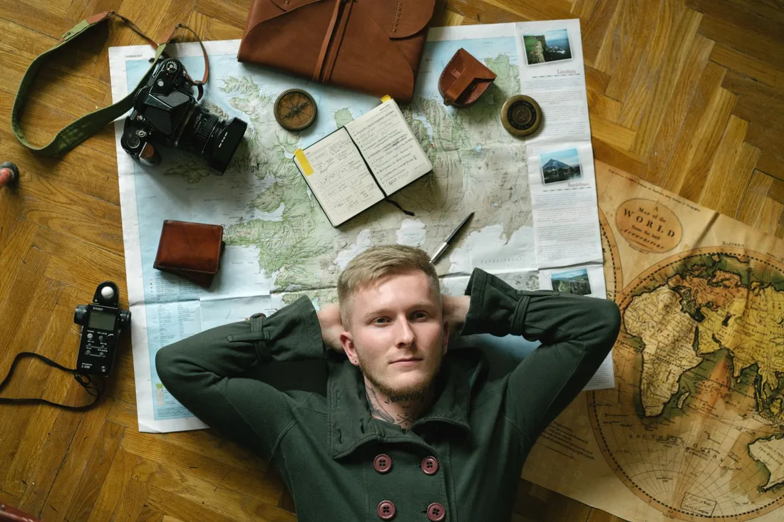 Jeune homme entouré de cartes, d'un appareil photo et d'un carnet, préparant un voyage