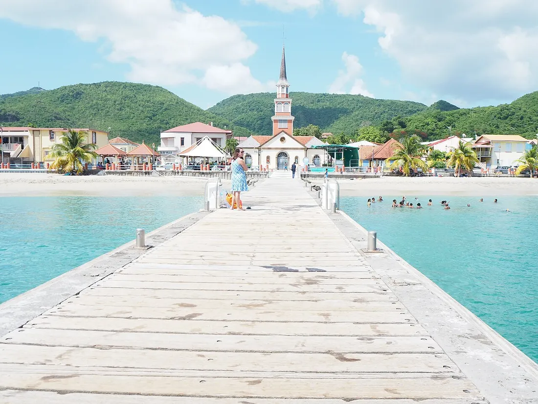 Ponton de bois menant au bourg des Anses-d'Arlet en Martinique, avec son église face à la mer turquoise et les collines verdoyantes en arrière-plan