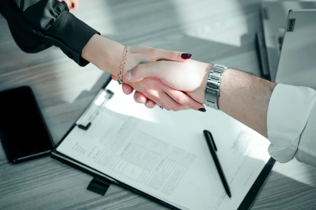 Poignée de main professionnelle au-dessus d'un contrat signé posé sur un porte-documents, avec stylo, symbolisant un accord d'entreprise