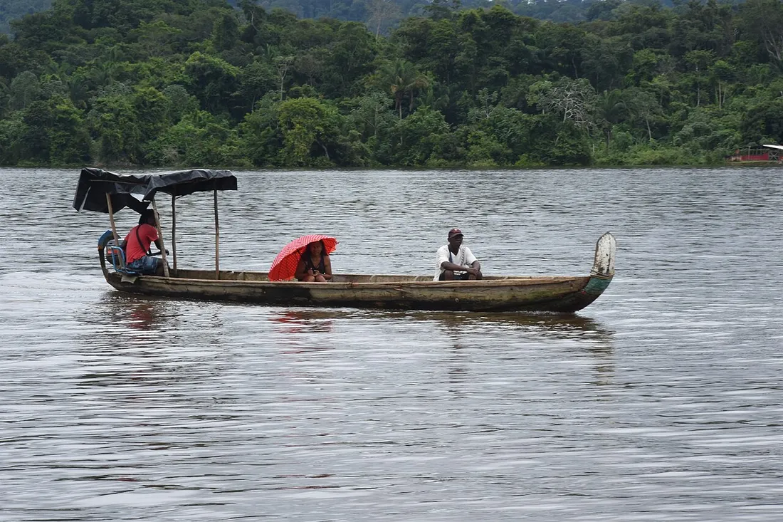 Pirogue traditionnelle naviguant sur le fleuve Maroni bordé de forêt en Guyane, voie de vie des communautés bushinengue
