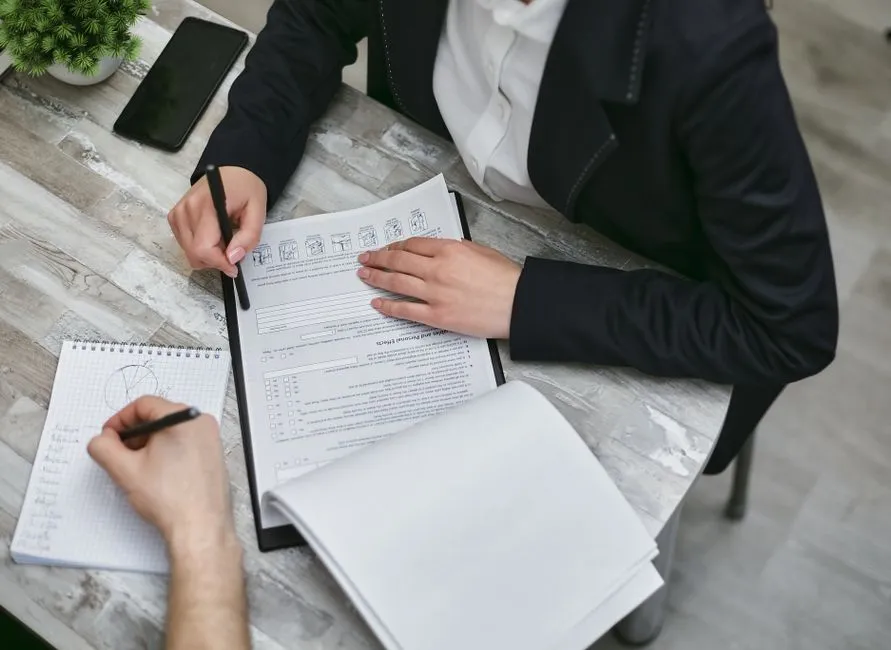 Deux personnes remplissent un formulaire administratif à un bureau, dossiers et checklist à la main