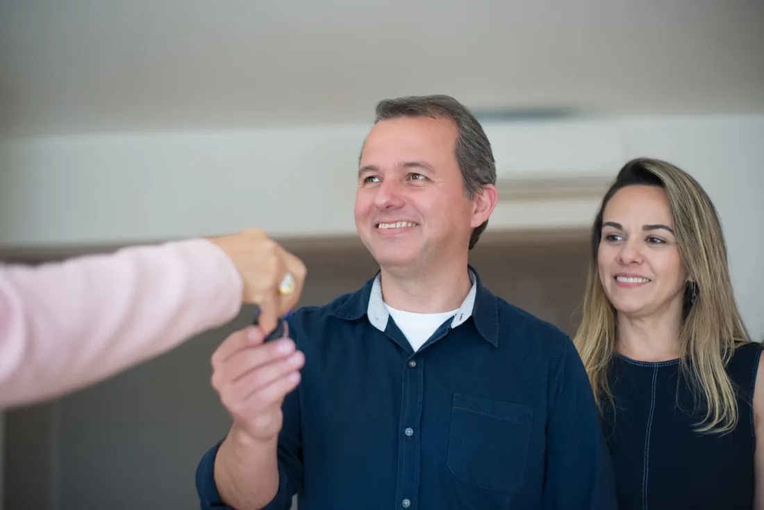 Un couple souriant reçoit les clés de son nouveau logement des mains d'un professionnel