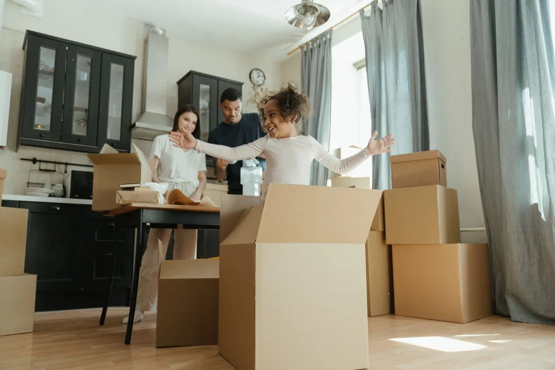 Famille avec un enfant déballant des cartons de déménagement dans la cuisine de leur nouveau logement