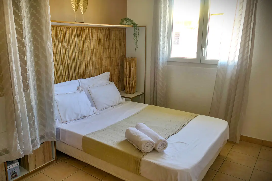 Chambre d'un appartement Cayenne Chic, lit double, tête de lit en bambou et serviettes roulées