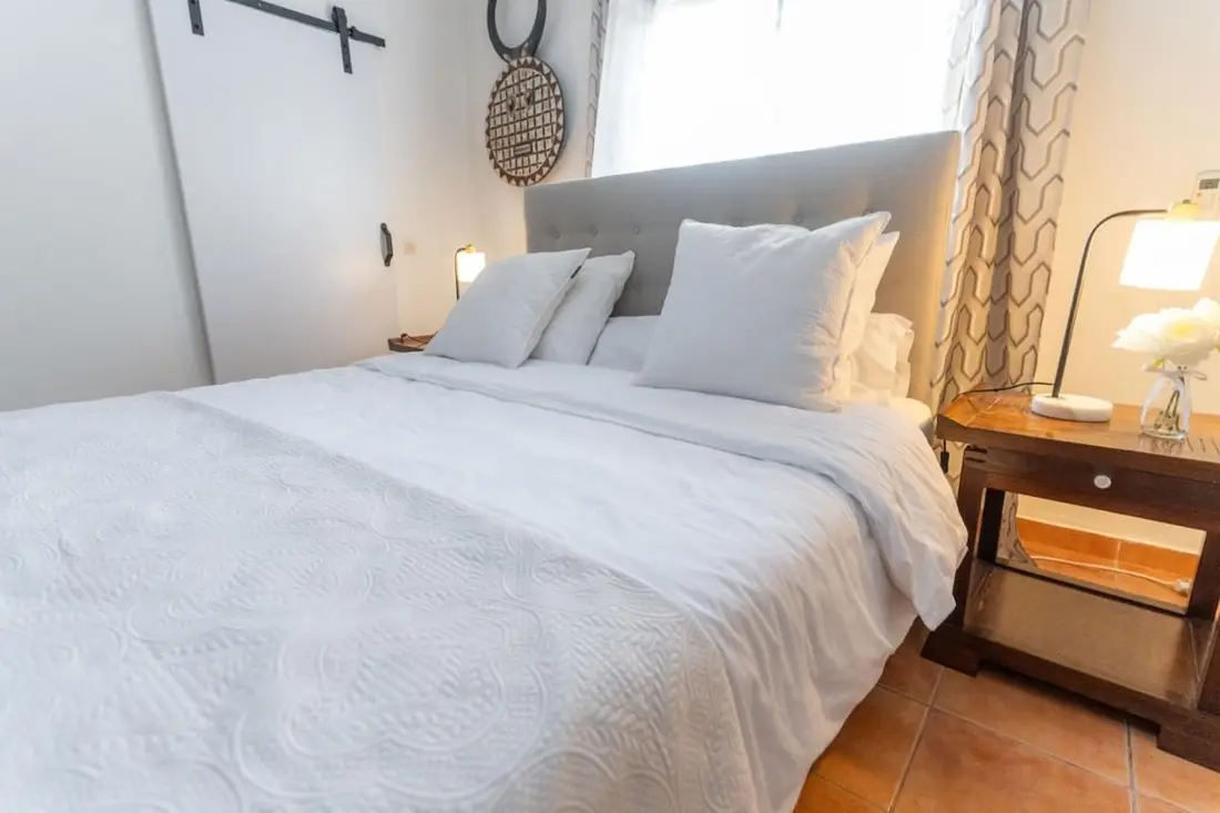 Chambre de la Casa Belas Artes : grand lit blanc à tête capitonnée, chevet en bois sombre et lampes allumées