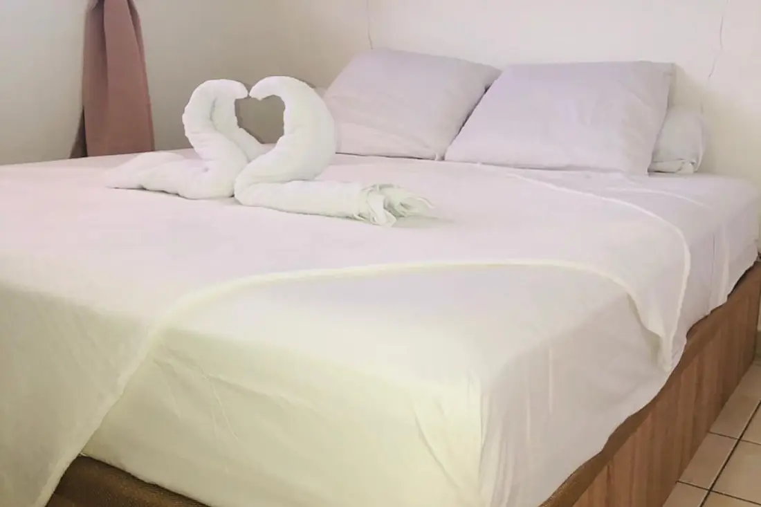 Lit du T2 Calme de Baduel : draps blancs et serviettes pliées en forme de cœur sur le couvre-lit