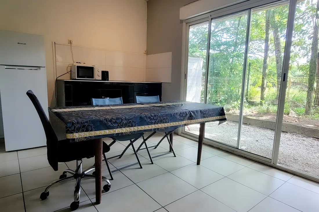 Salle à manger de la Villa Mahury : grande table à nappe bleue face à la baie vitrée ouverte sur le jardin