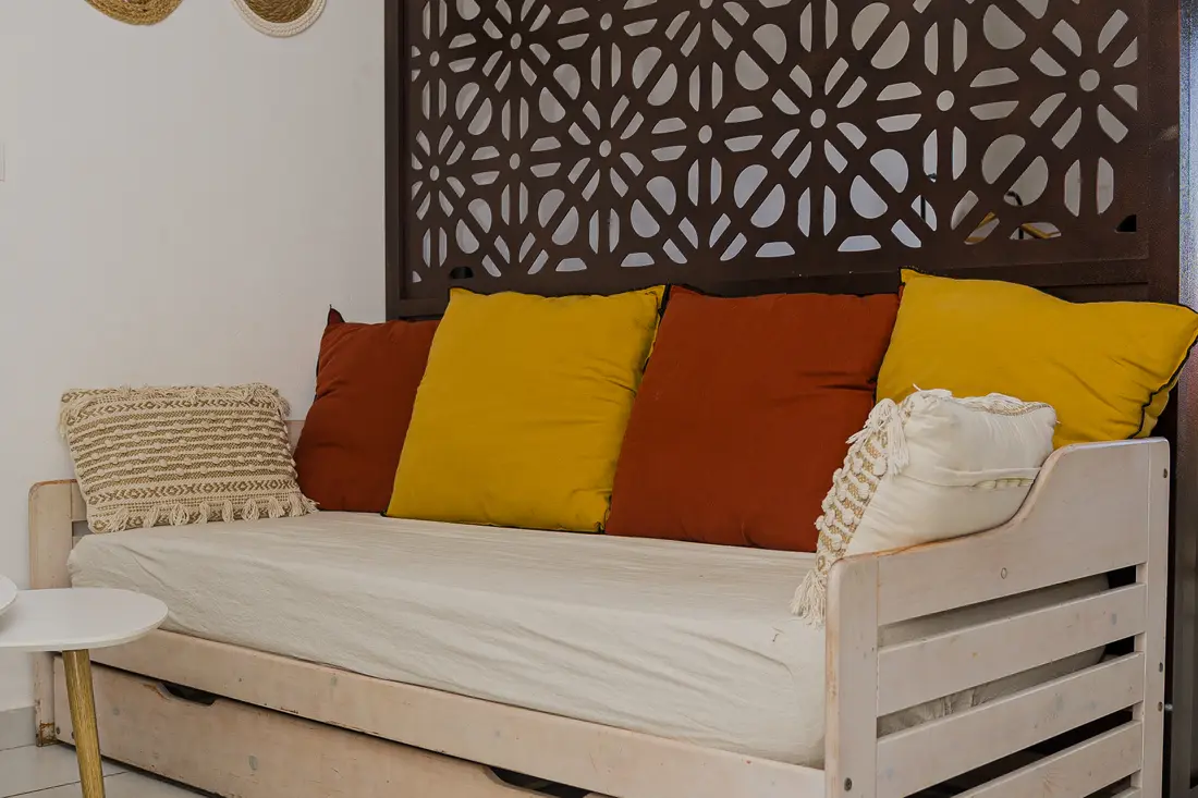 Banquette du Cocon Cayennais : coussins jaunes et terracotta devant un claustra en bois sombre à motifs floraux