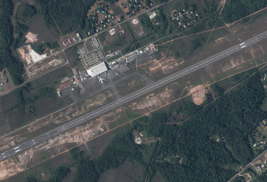 Vue aérienne verticale de l'aéroport Félix-Éboué à Matoury : aérogare, aire de stationnement avec avions et piste unique traversant l'image en diagonale