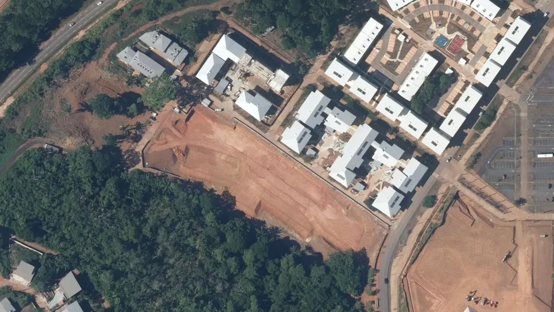 Orthophotographie aérienne de la rue Simone Fléret Farlot, dans l'écoquartier Georges Othily à Rémire-Montjoly : immeubles collectifs à toitures claires, parcelle décapée en attente de construction et lisière de forêt