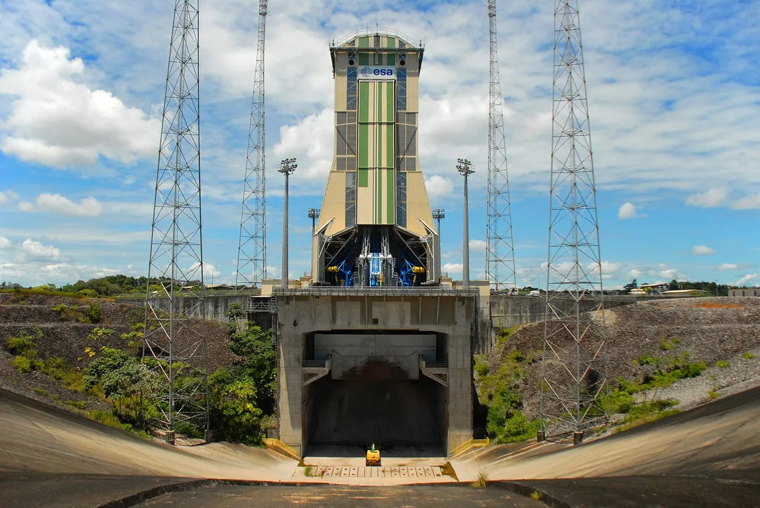 Ensemble de lancement Soyouz du Centre spatial guyanais vu depuis le carneau de déflexion des jets : tranchée bétonnée au premier plan, portique mobile beige et vert dressé au-dessus du pas de tir, encadré de quatre pylônes paratonnerres