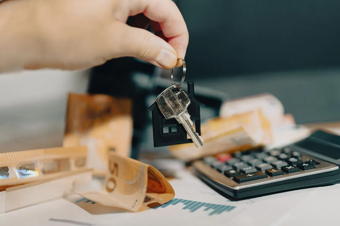 Main tenant des clés au-dessus de billets et d'une calculatrice