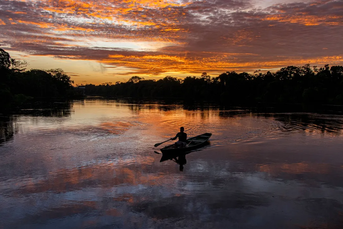 Piroguier remontant une rivière amazonienne au coucher du soleil