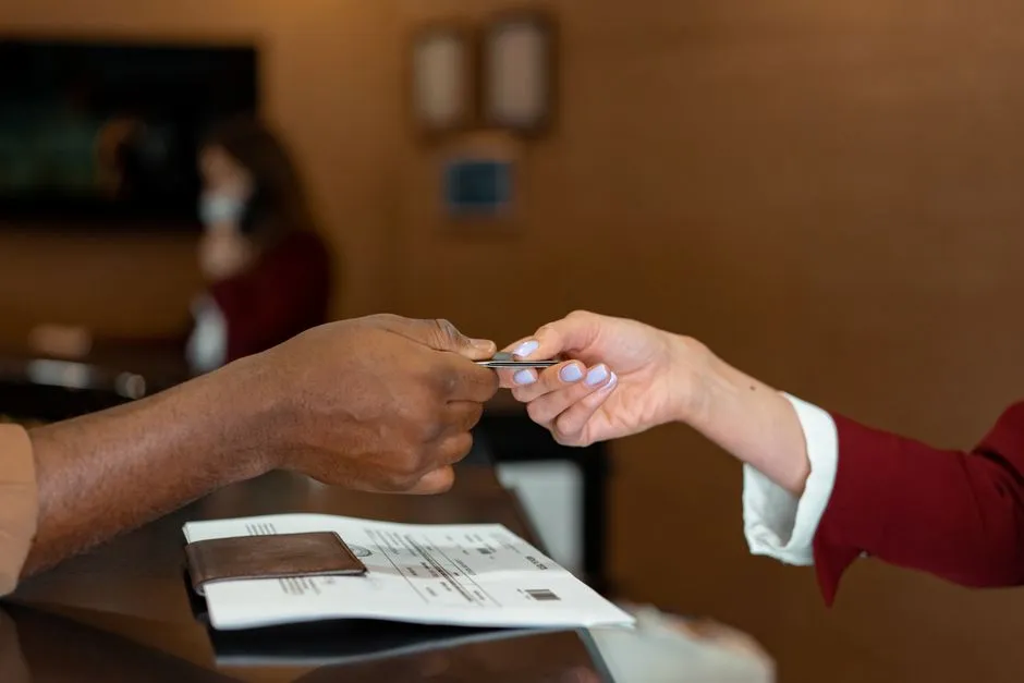 Client d'affaires tendant sa carte bancaire à une réceptionniste d'hôtel, une facture posée sur le comptoir