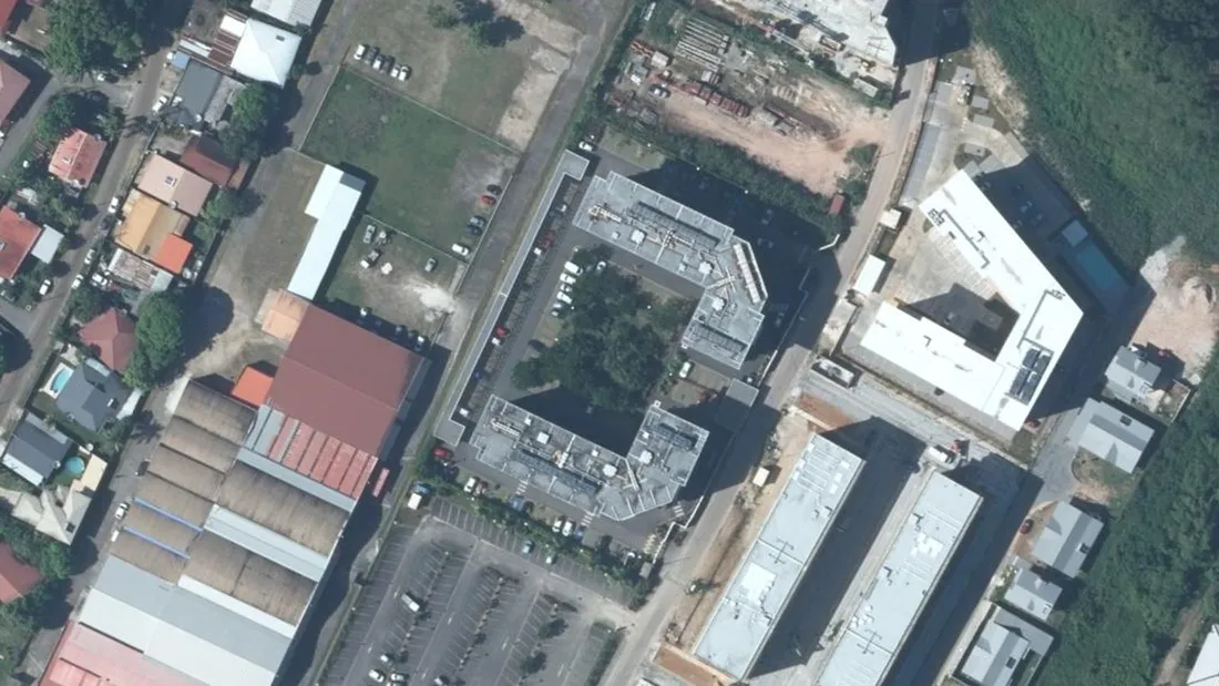 Vue aérienne verticale de l'îlot de la rue de l'Union, quartier de Baduel à Cayenne : deux bâtiments de logements en U autour d'une cour plantée et de leurs places de stationnement, entourés de hangars d'activité
