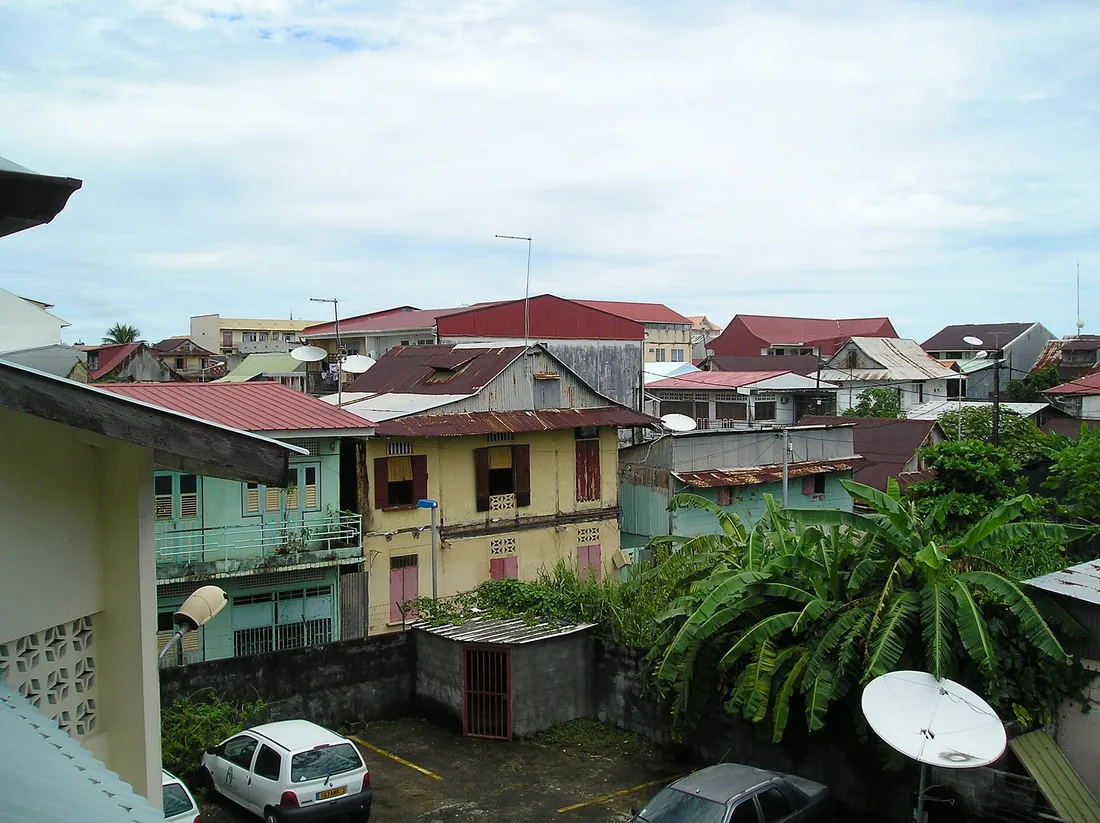 Les toits du centre de Cayenne vus depuis un étage : toitures de tôle rouillées, cases créoles en bois, petits immeubles, antennes paraboliques et cour de stationnement