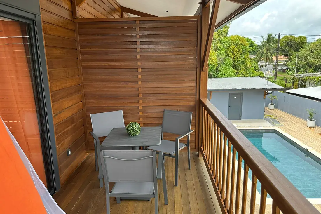 Balcon en bois d’un logement de la Résidence Francis : table et chaises grises, garde-corps ouvrant sur la piscine de la résidence