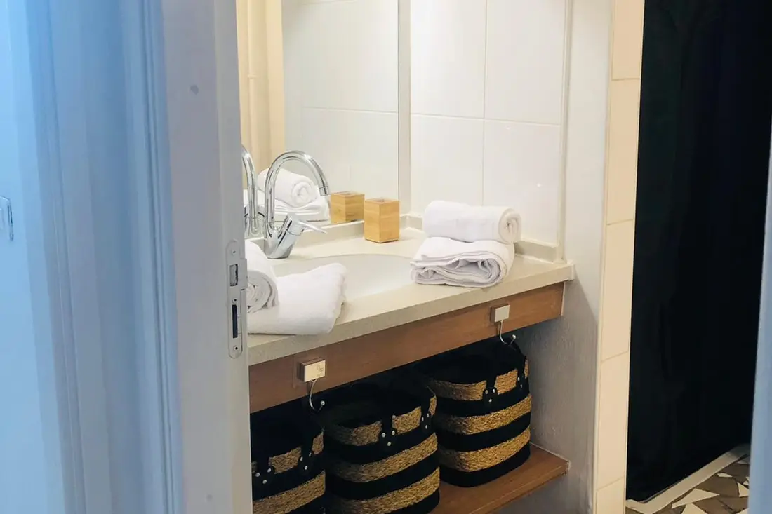 Banheiro de uma acomodação em Caiena com pia, espelho e toalhas dobradas em cestos