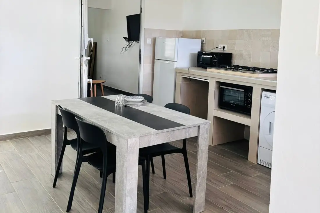 Salle à manger et cuisine de la Tropikana : table grise, chaises noires, plaques gaz et four sous le plan carrelé