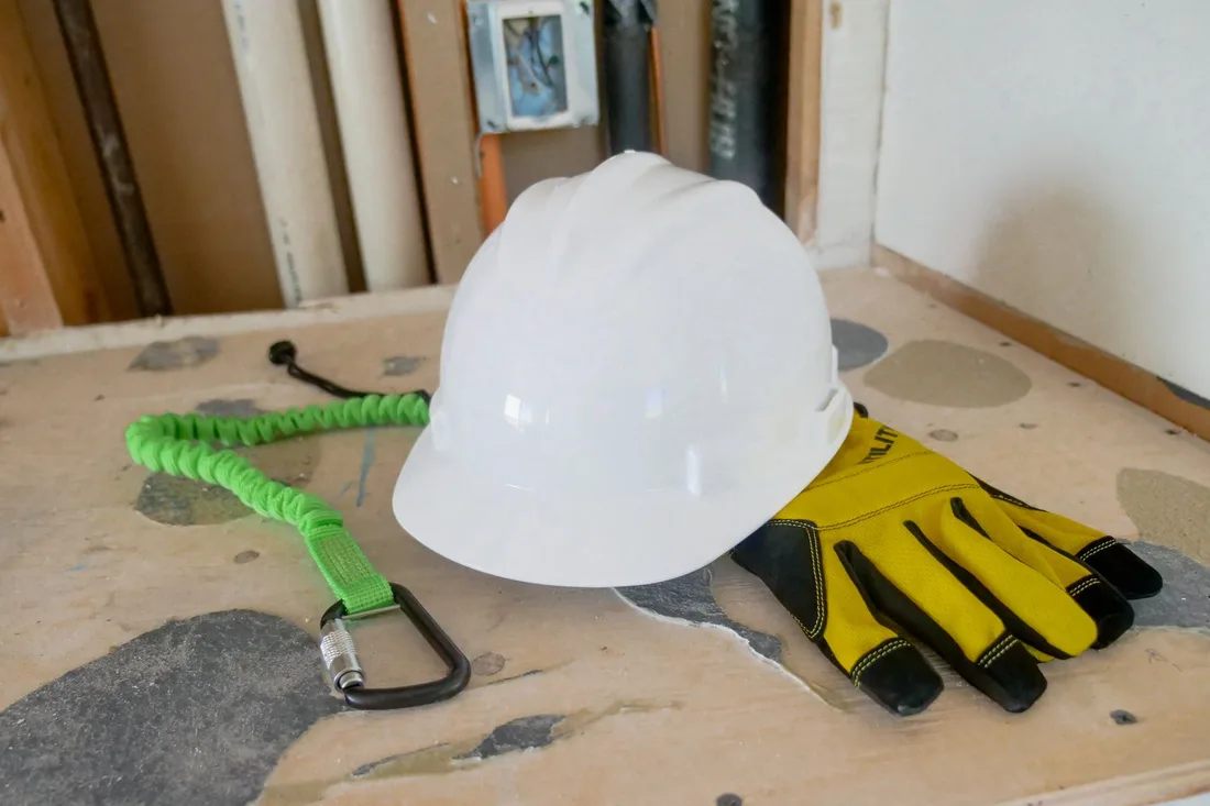 Casque de chantier blanc, gants de protection et harnais de sécurité posés côte à côte