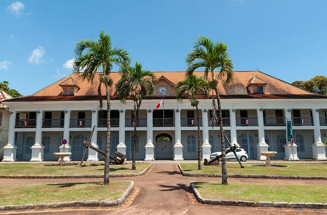 Façade de l'hôtel de préfecture de la Guyane à Cayenne, bâtiment colonial à colonnades et drapeau français, entouré de palmiers