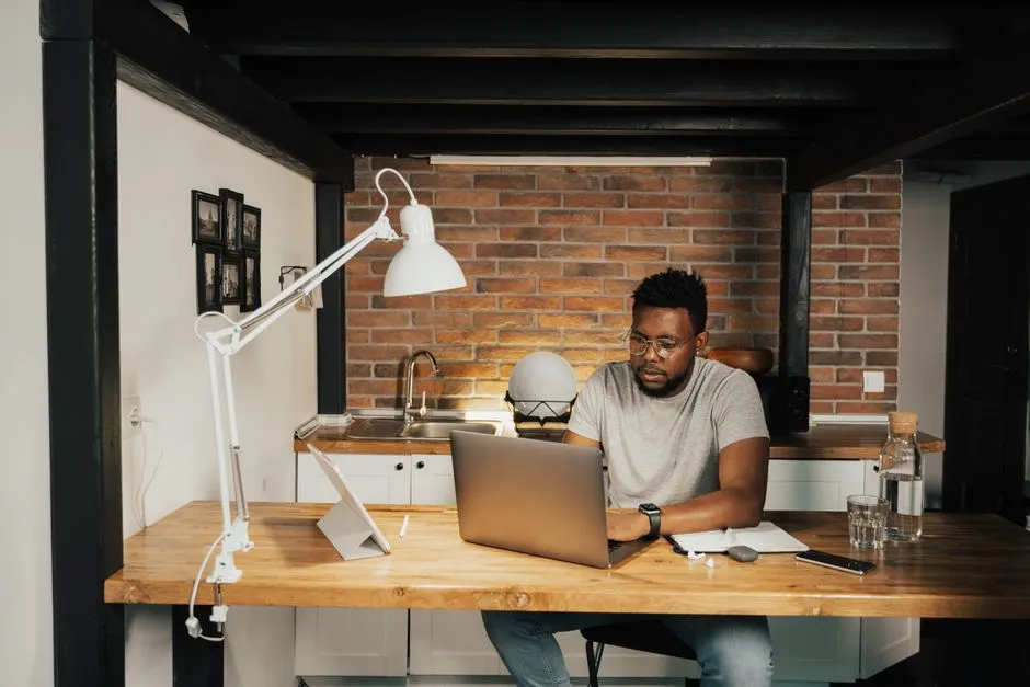 Homme en déplacement professionnel travaillant sur son ordinateur portable à la grande table d'un logement meublé équipé d'une cuisine