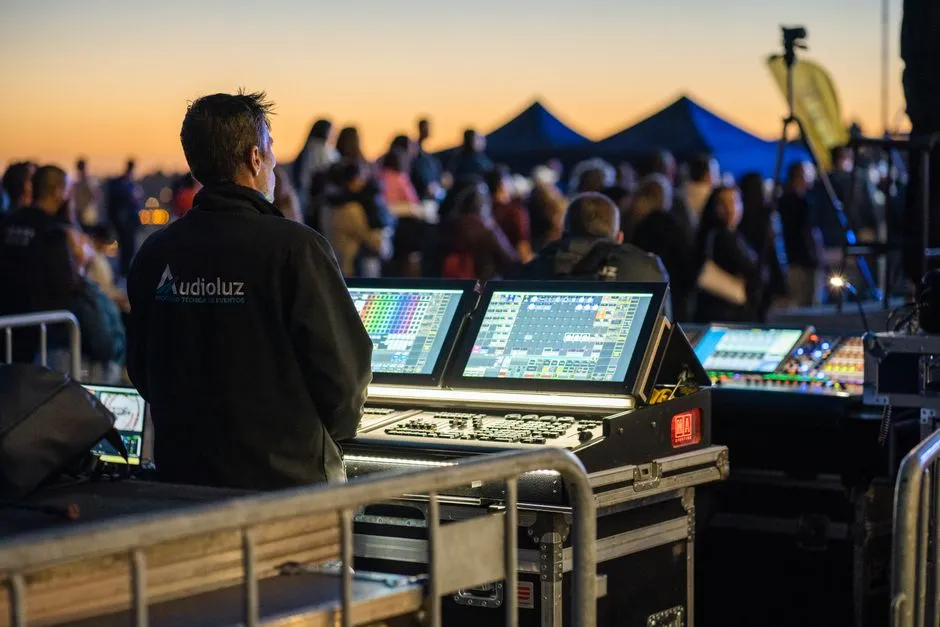 Technicien son et lumière d'un prestataire événementiel derrière sa console de régie lors d'un événement en plein air au crépuscule