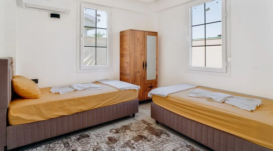 Chambre lumineuse d'un logement meublé équipée de deux lits simples, d'une armoire et de serviettes pliées, adaptée à l'hébergement de deux membres du staff