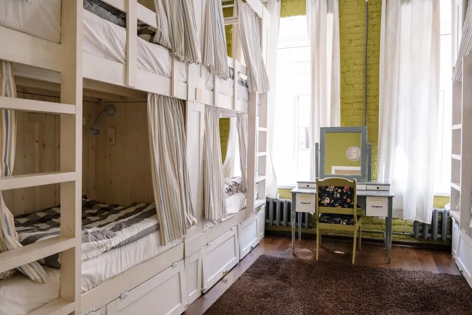 Chambre d'hébergement collectif avec lits superposés en bois, rideaux d'intimité et rangements individuels