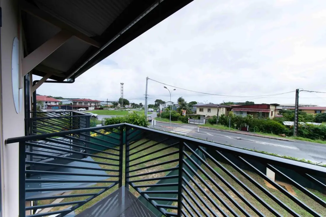 Vue depuis le balcon du Baduel Smart Studio sur une rue du quartier Baduel à Cayenne, garde-corps à lames vertes au premier plan