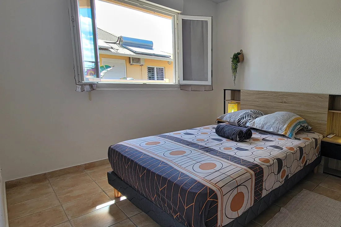 Chambre d'un appartement Cayenne Chic à Cayenne, lit fait et fenêtre donnant sur la végétation
