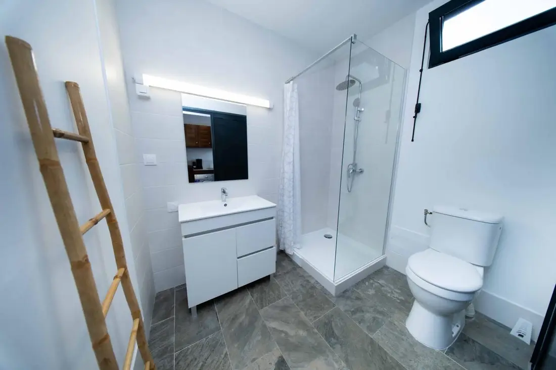 Salle d’eau du Baduel Smart Studio : douche vitrée, vasque blanche et échelle en bambou décorative
