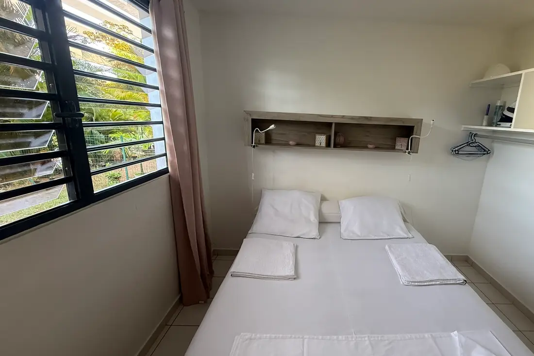 Chambre du Diamant Cayennais à Baduel : lit double aux serviettes pliées, fenêtre à persiennes ouvrant sur la verdure