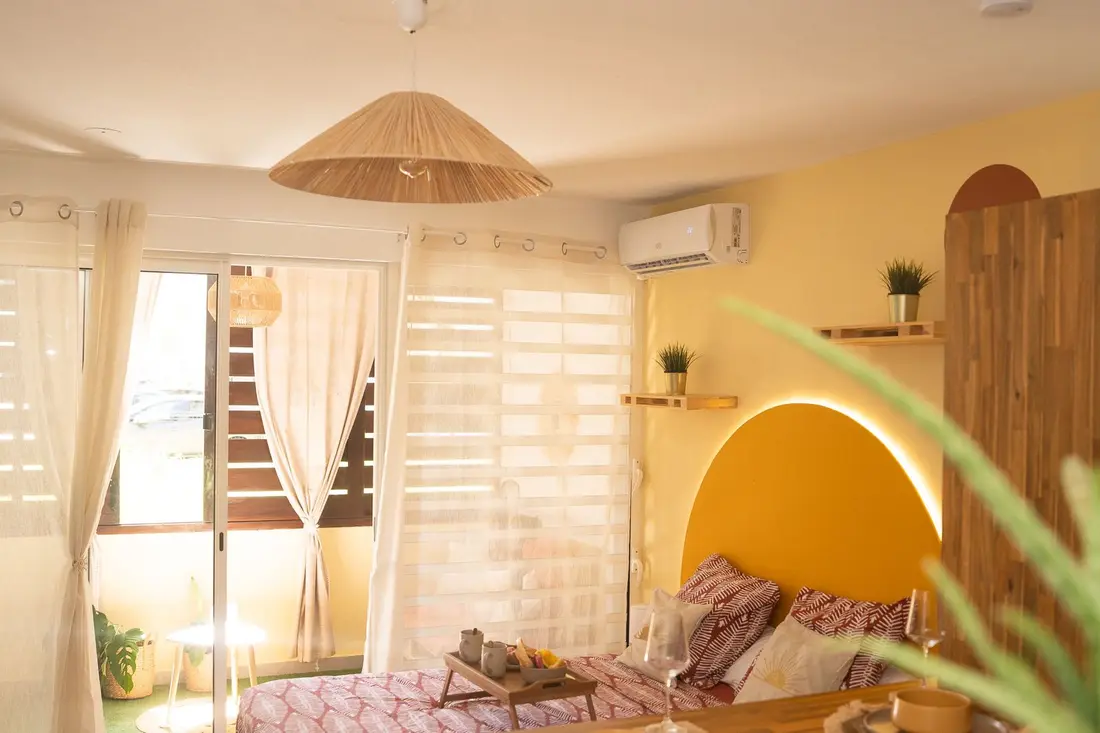 Chambre du Cocon Chic à Cayenne : climatiseur mural au-dessus du lit, tête de lit en arche jaune rétroéclairée