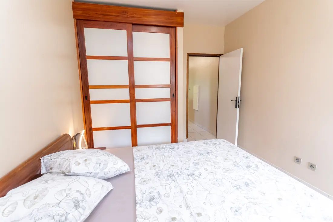 Chambre du T2 Mahury à Rémire-Montjoly, lit double et porte coulissante en bois