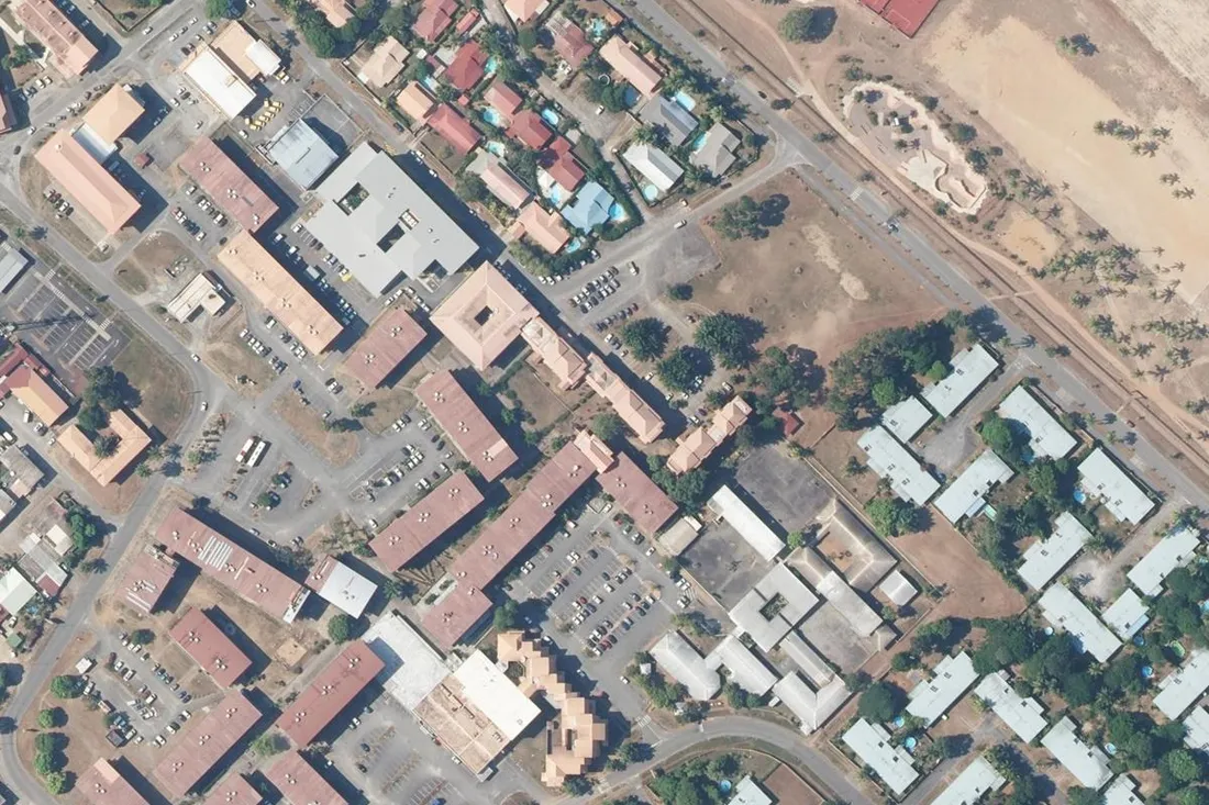 Vue aérienne verticale d'un quartier d'immeubles collectifs de Kourou, en Guyane : barres de logements à toitures rouges, parkings et pavillons, au nord-est de la commune